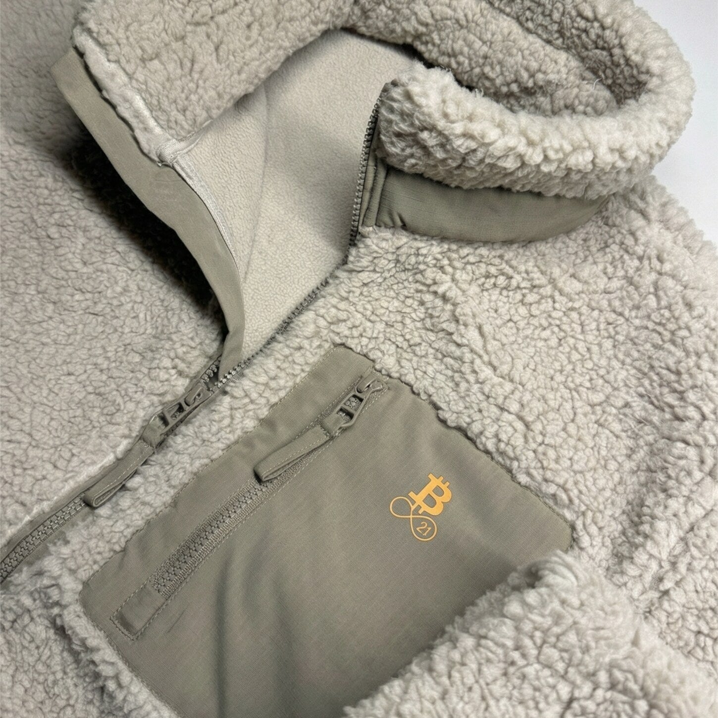 Bitcoin Sherpa-Jacke beige Detailaufnahme der Brusttasche mit Bitcoin21 Logo-Stickerei