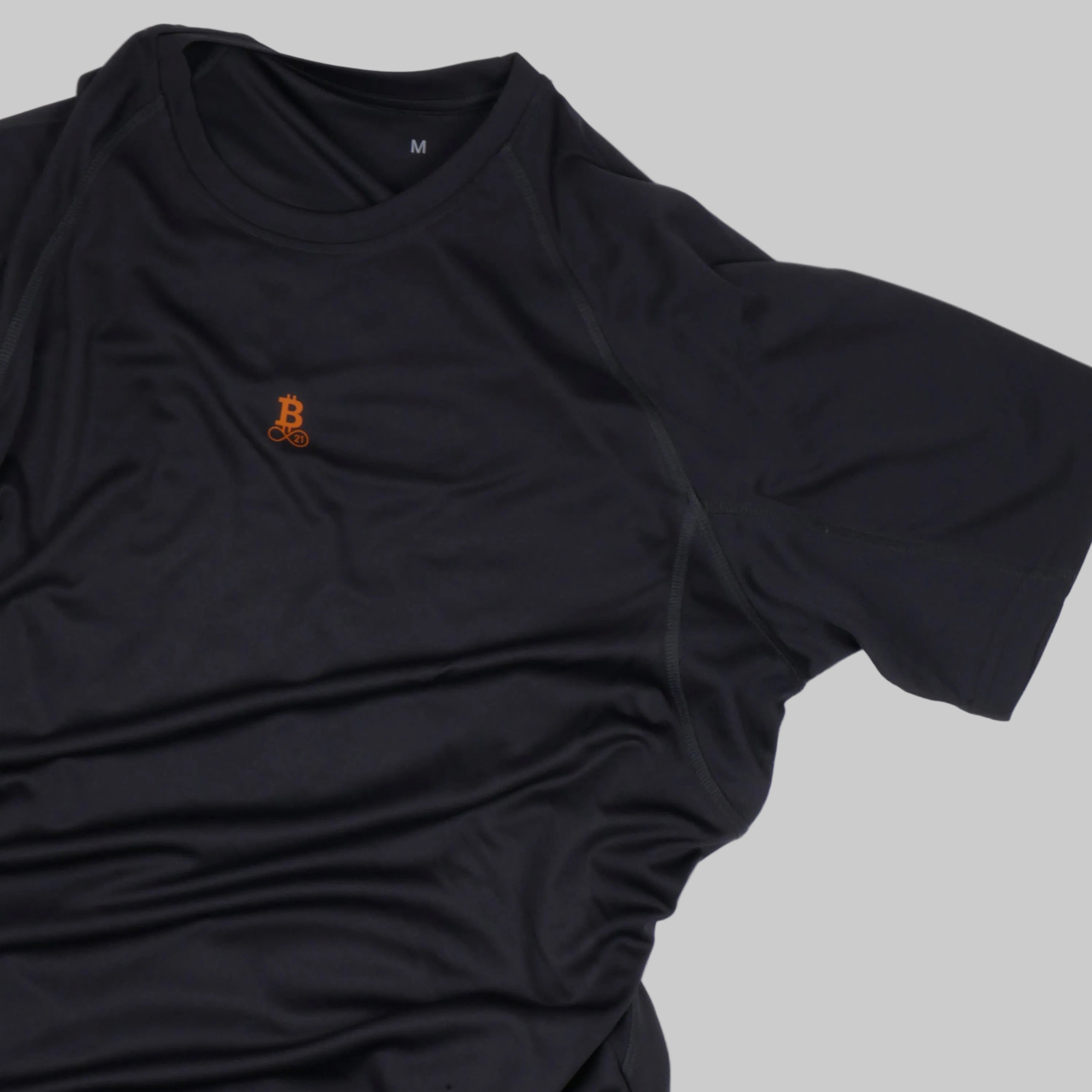 Bitcoin hardloopshirt Hal Finney in donkergrijs, detailopname van de voorkant met klein oranje Bitcoin21-logo en raglanmouw