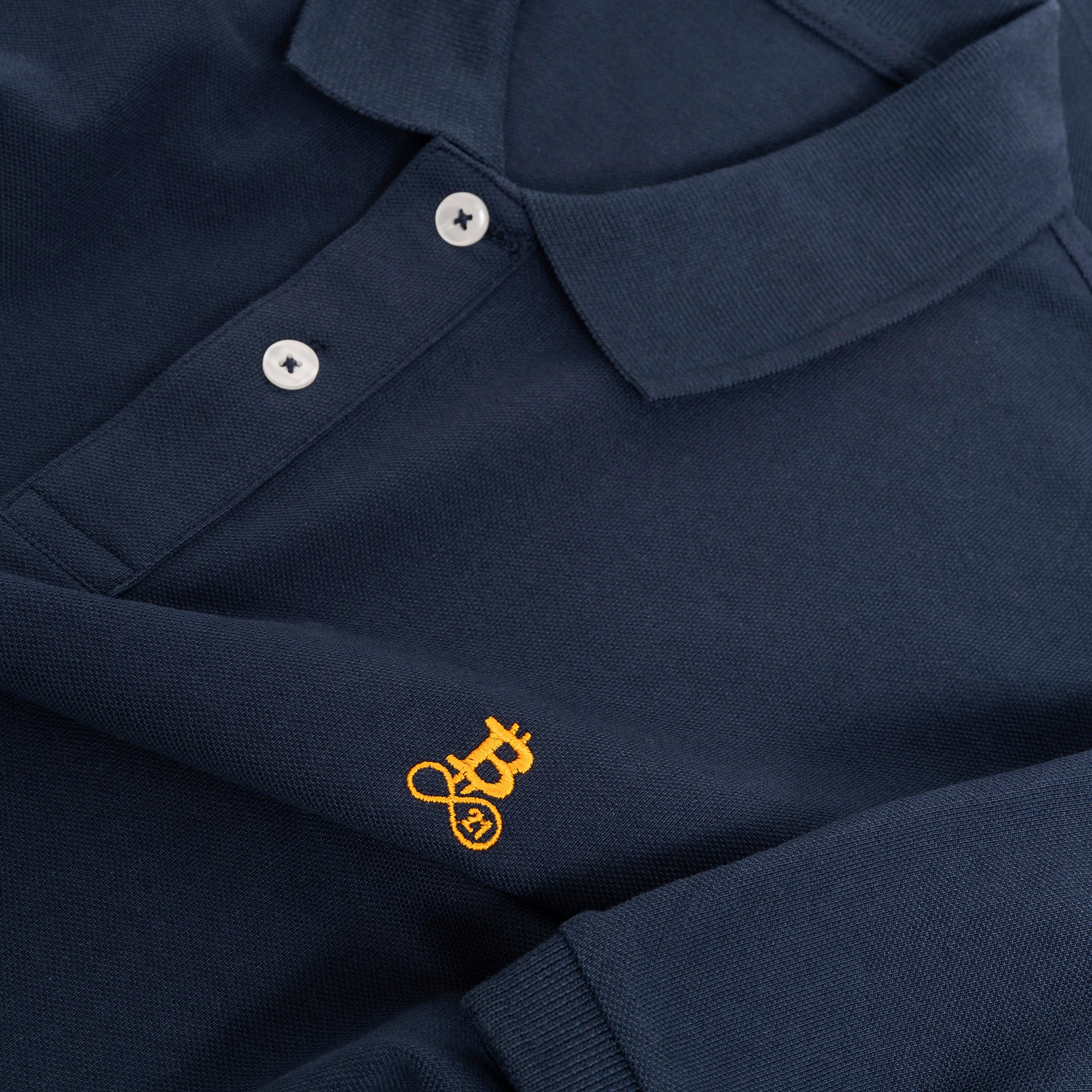 Polo Bitcoin navy da uomo in cotone, dettaglio di colletto polo, placket e logo Bitcoin21 ricamato in arancione