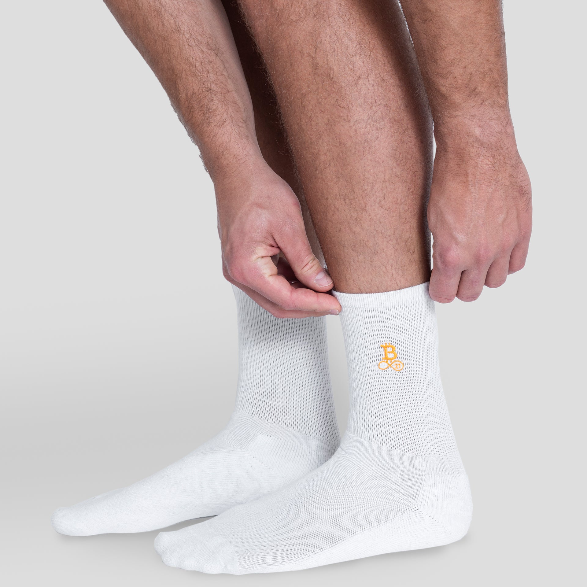 Calzini Bitcoin bianco da uomo con logo arancione Bitcoin21 sul gambale, il modello indossa i calzini crew e sistema il polsino a coste elastico