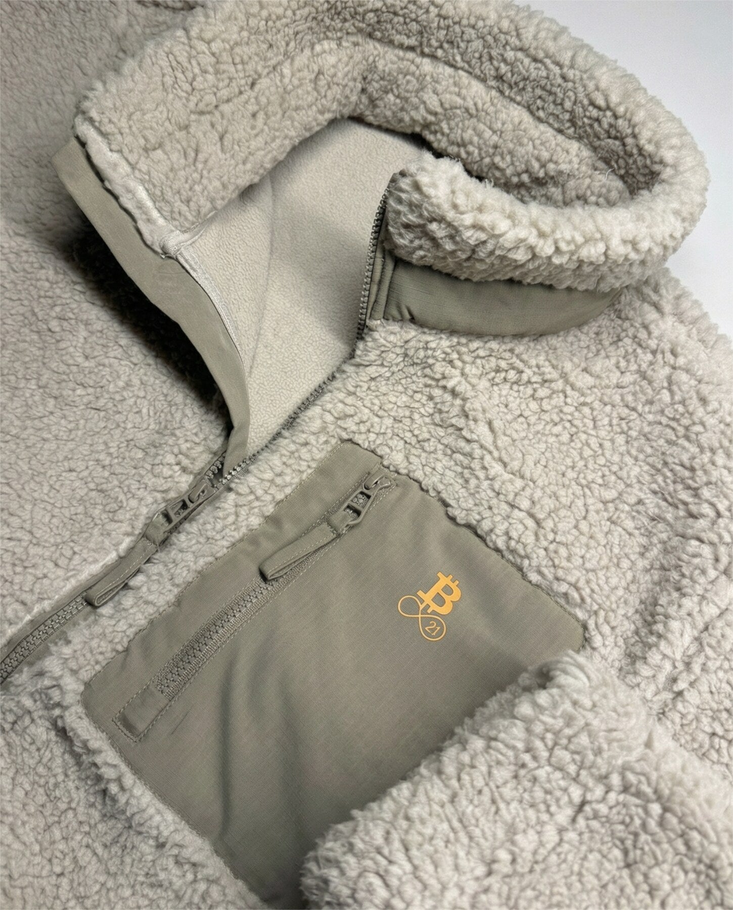 Bitcoin Sherpa-Jacke beige Detailaufnahme der Brusttasche mit Bitcoin21 Logo-Stickerei