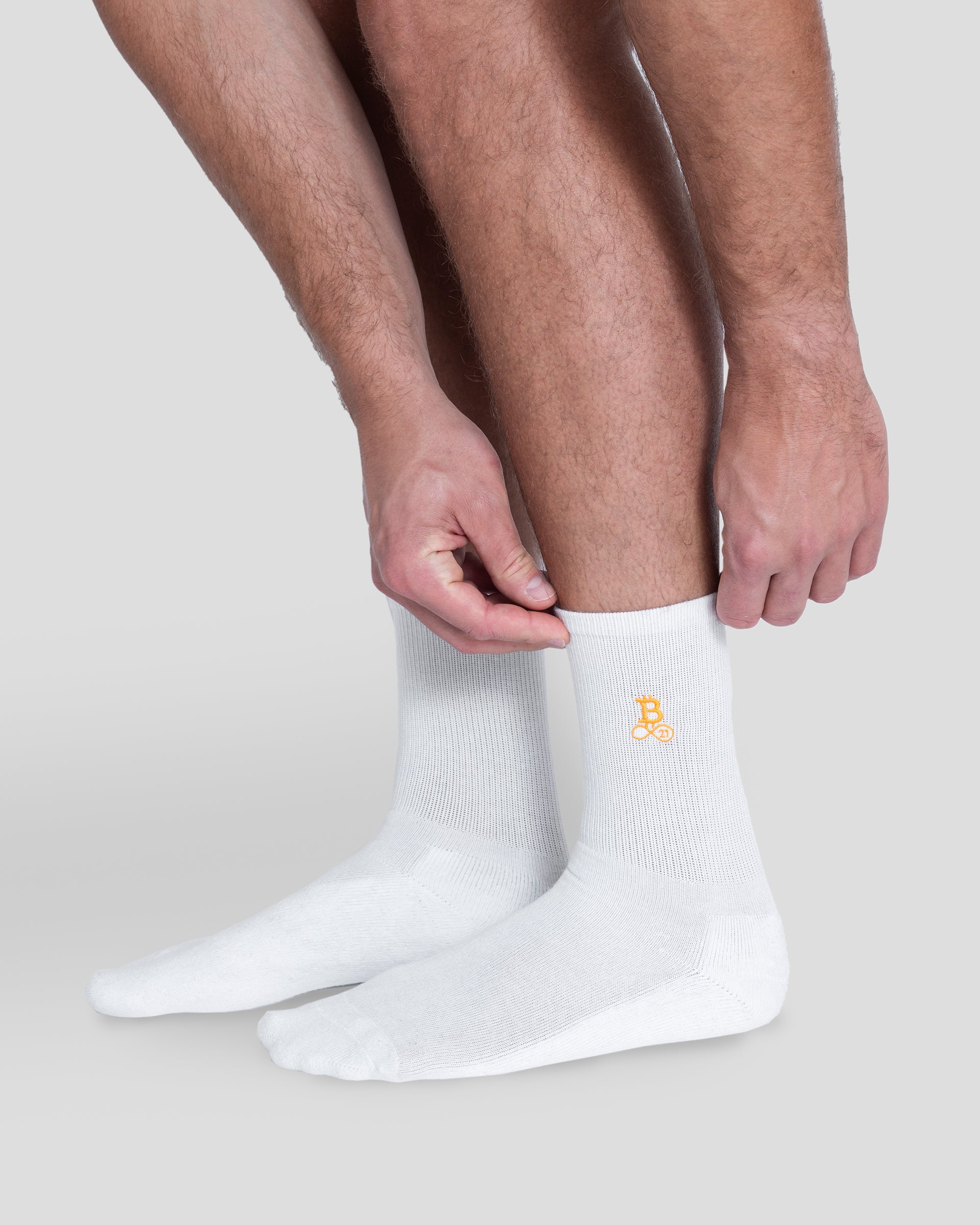Bitcoin Socken weiß für Herren mit orangefarbenem Bitcoin21 Logo auf dem Schaft, Model trägt die Crew Socken und richtet das elastische Rippbündchen