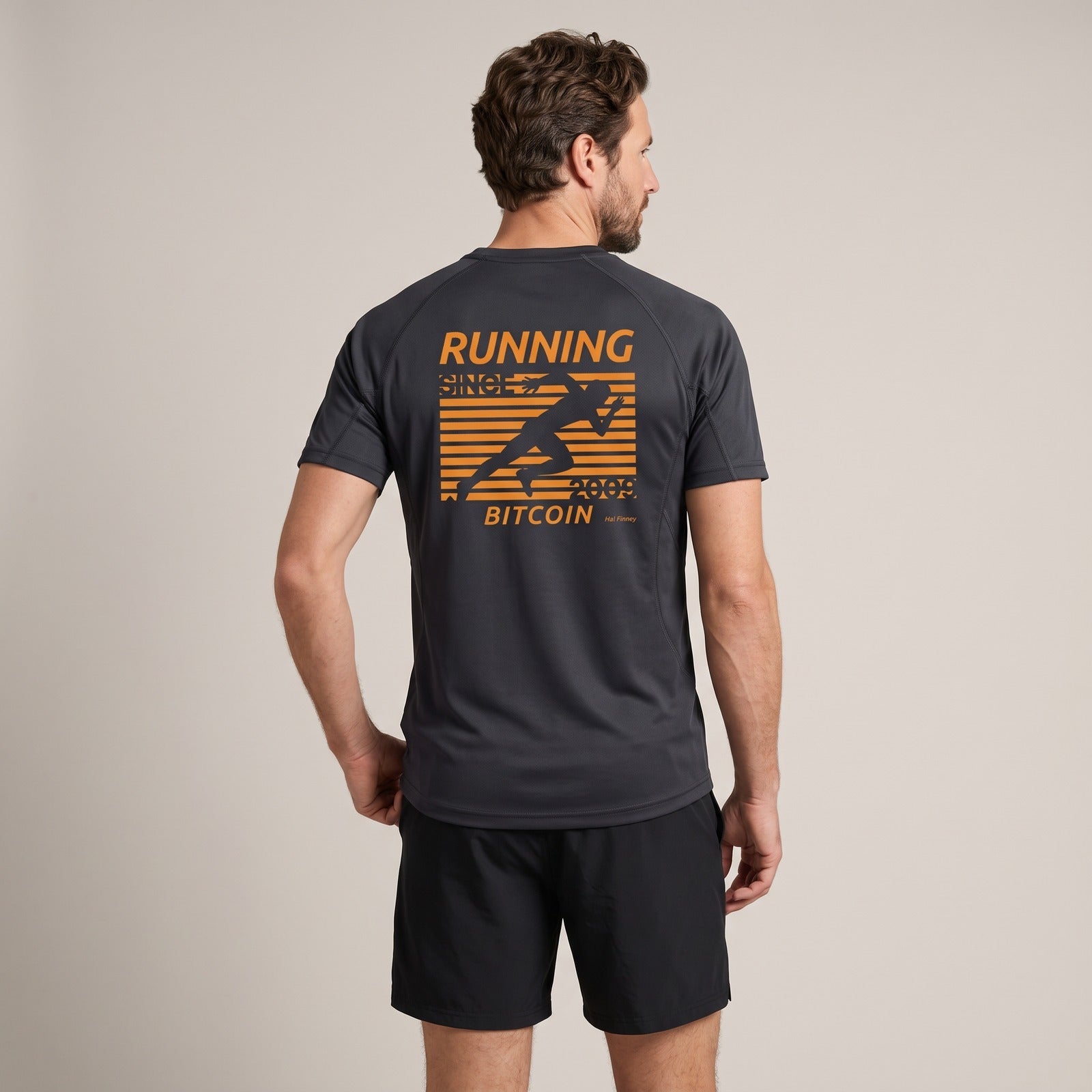 Man draagt het Bitcoin hardloopshirt Hal Finney in donkergrijs, rugprint met oranje hardloper, RUNNING BITCOIN, 2009 en Hal Finney